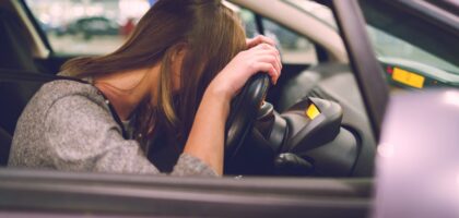 A women is slumped over the steering wheel as though she is in actual physical control while under the influence