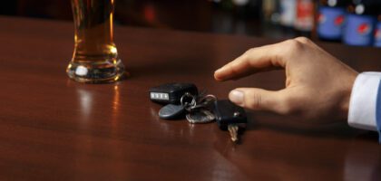 A man's hand reaching for car keys near a glass of beer at a bar. Avoid aggravated DUI.